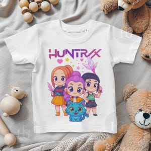 Pu&ograve; includere: T-shirt bianca con la scritta "HUNTRAX" in viola e una grafica di tre ragazze dei cartoni animati e un gatto blu. Le ragazze indossano gonne e tengono in mano oggetti a forma di cristallo. La maglietta &egrave; realizzata in un materiale morbido e confortevole.