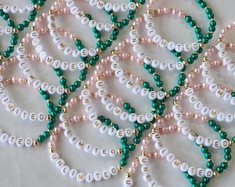 Può includere: Primo piano di un mucchio di braccialetti con perline bianche che compongono la scritta "UNLIMITED" in lettere dorate. I braccialetti sono infilati su perline verdi e rosa.