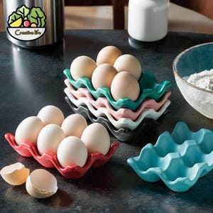 May include: Six ceramic egg holders in various colors, including red, pink, blue, and green. The holders are stacked on top of each other, with the top holder containing six white eggs.