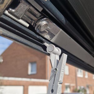 Peut inclure: Gros plan d'une pince à linge grise avec le texte "Diplom Bastler" fixée à un auvent noir. L'auvent comporte une pièce en plastique blanc et une charnière métallique. Une voiture est visible en arrière-plan.