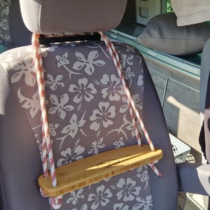 Könnte beinhalten: Ein weißes Seil mit roten Streifen hängt an der Kopfstütze eines Autositzes. An dem Seil ist ein Holztablett befestigt. Der Autositz hat ein graues und weißes Blumenmuster.