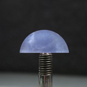 May include: A translucent, half-dome shaped gemstone in shades of blue and white, mounted on a silver metal post. The gemstone has a smooth, polished surface and is set against a dark background. The overall effect is one of elegance and simplicity.