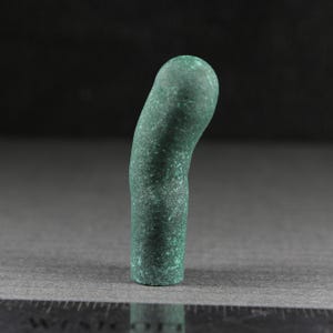 Puede incluir: Objeto cilíndrico curvado con una superficie verde texturizada y moteada. El objeto tiene una parte superior redondeada y una base plana. El color es un verde intenso y apagado con variaciones de verde claro y marrón.