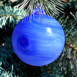 May include: A blue glass Christmas ornament with white swirls. The ornament is hanging on a green Christmas tree.