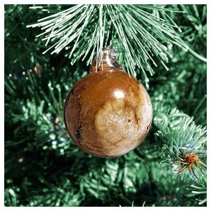 May include: A brown glass Christmas ornament with a white marbled design. The ornament is hanging on a green artificial Christmas tree.