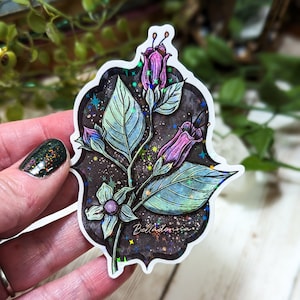 May include: A holographic sticker featuring a purple and green illustration of a belladonna plant with the word "Belladonna" written on the sticker.