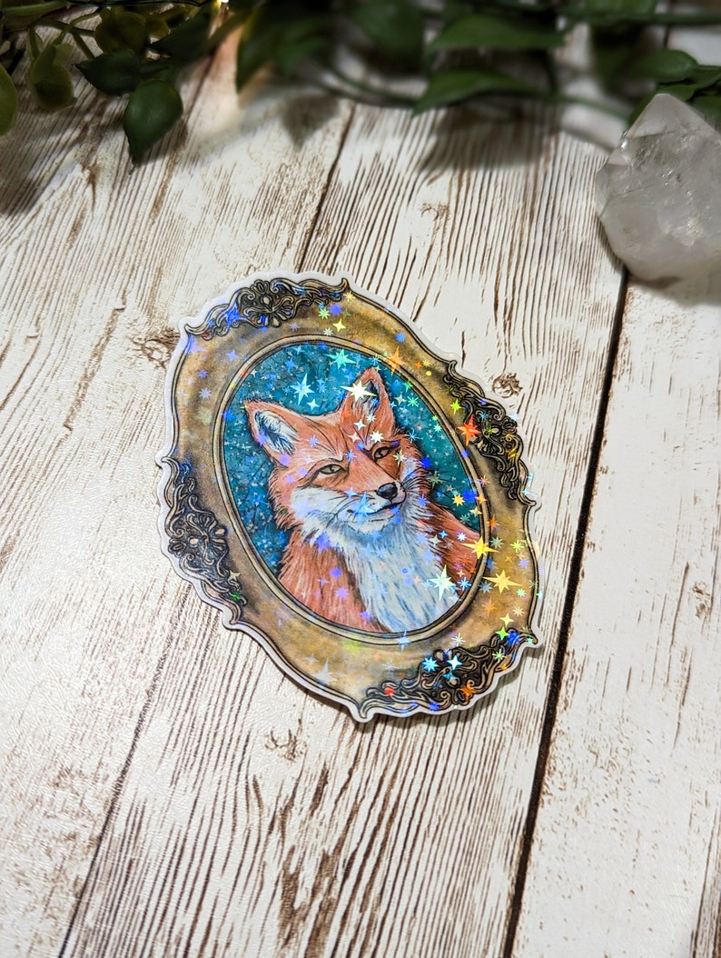 K&ouml;nnte beinhalten: Ein holografischer Aufkleber mit einem roten Fuchs in einem goldenen, verzierten Rahmen vor einem blauen Sternenhimmel.