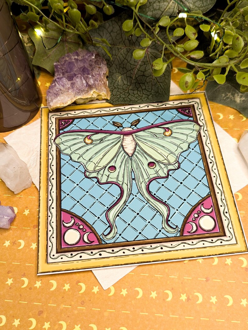 Peut inclure: Impression d'art carr&eacute;e repr&eacute;sentant un papillon lune. Le papillon a des ailes vert p&acirc;le avec des accents roses et violets, sur un fond bleu clair &agrave; motif de losanges. L'impression est encadr&eacute;e d'une bordure jaune et d'&eacute;l&eacute;ments d&eacute;coratifs.