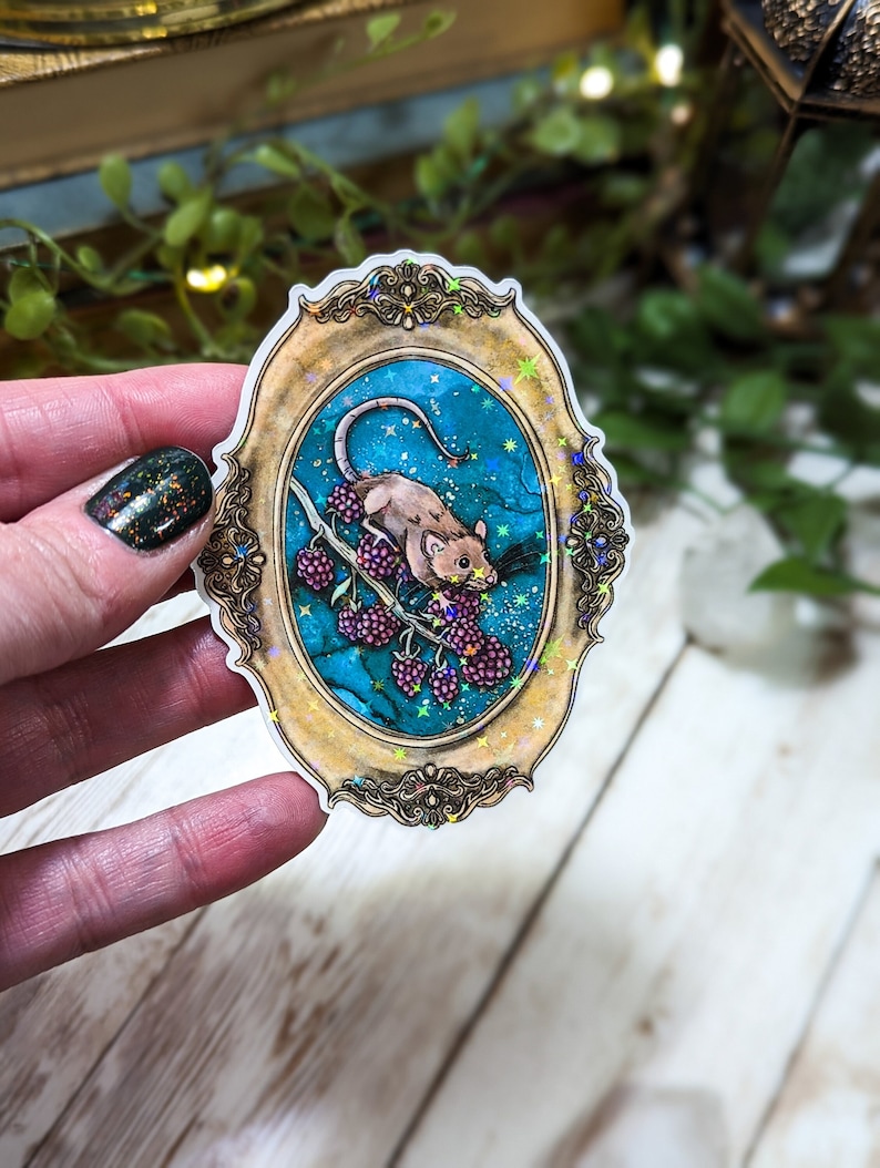 May include: A sticker featuring a whimsical illustration of a mouse eating berries on a branch, set against a starry night sky. The image is framed in a gold ornate frame with a glittery finish.