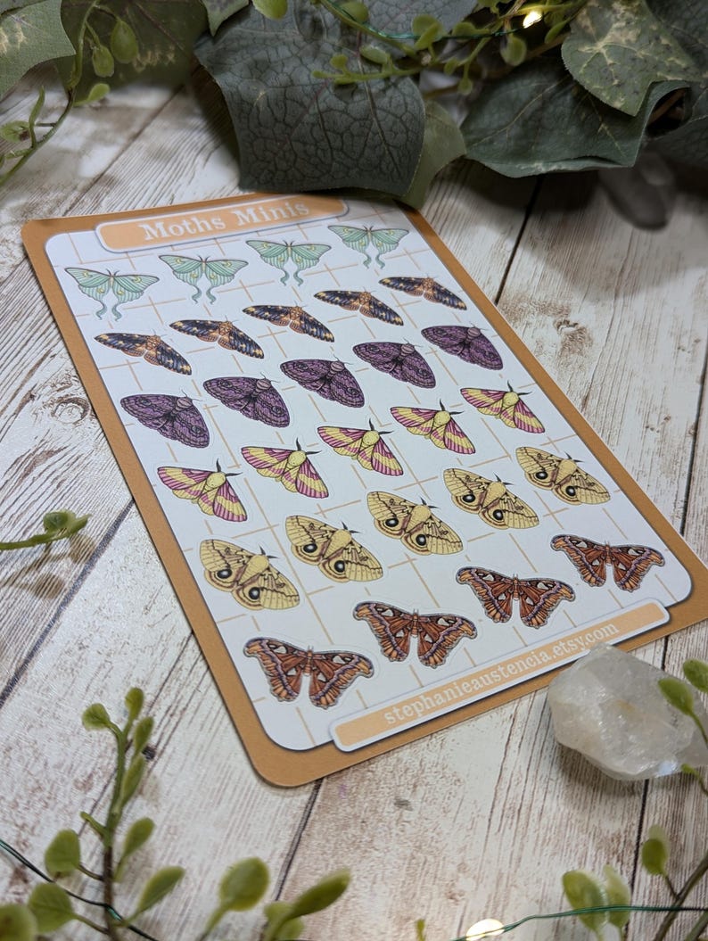 May include: A sheet of colorful moth stickers with a grid pattern. The stickers feature various moth species in shades of green, purple, yellow, and orange. The sheet is labeled "Moths Minis" and includes the Etsy shop name "stephanie austencla.etsy.com".