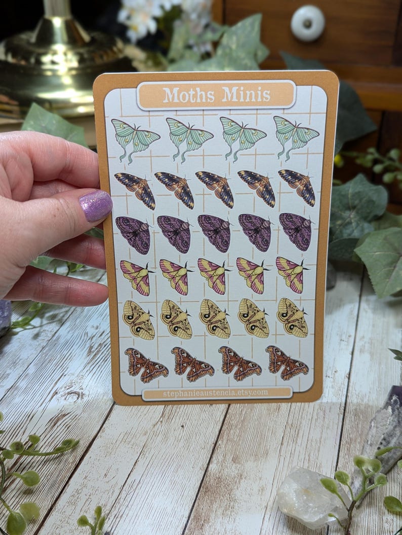 May include: A sheet of stickers featuring various moth illustrations. The stickers are arranged in a grid pattern on a white background with a light brown border. The title "Moths Minis" is printed at the top of the sheet. The text "stephanielaustencia.etsy.com" is printed at the bottom of the sheet.
