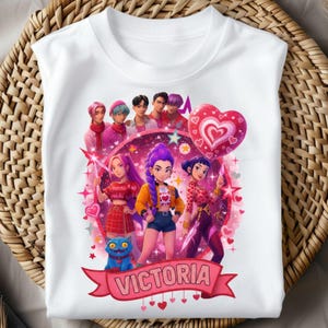 May include: White t-shirt featuring a colorful graphic of a group of animated characters, a blue cat, and the name "Victoria" on a banner. The design includes hearts and stars, with a pink and purple color scheme.