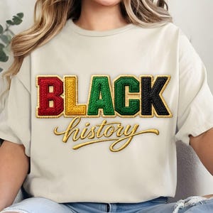 Op de afbeelding: Crèmekleurig T-shirt met de woorden "BLACK history" geborduurd in kleur. Het woord "BLACK" is in rood, geel, groen en zwart, met "history" in een gouden script. Het shirt heeft korte mouwen.