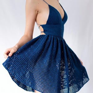 Könnte beinhalten: Ein dunkelblaues Häkelkleid mit tiefem V-Ausschnitt, dünnen Spaghettiträgern und einem rückenfreien Design mit seitlichen Bindebändern. Das Oberteil ist dicht gehäkelt, während der ausgestellte Rock ein offenes, gitterartiges Häkelmuster aufweist.