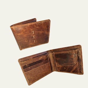 Puede incluir: Dos carteras de cuero marrón. Una está abierta, revelando ranuras para tarjetas y un bolsillo. La otra está cerrada, con tres puntadas verticales en la parte delantera. Ambas carteras muestran desgaste, con grano y textura visibles.