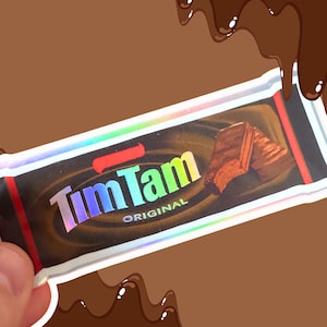 Pode incluir: Uma imagem em close-up da embalagem de uma barra de chocolate Tim Tam Original. A embalagem é preta com o logotipo Tim Tam em cores iridescentes. A embalagem também apresenta uma imagem do biscoito de chocolate e a palavra "ORIGINAL".