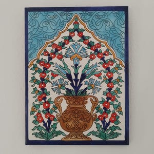 Peut inclure: Carreau de céramique rectangulaire avec une bordure bleu foncé. Le carreau présente un motif central d'un vase marron rempli de fleurs bleues et rouges. Le fond est blanc avec un dessus décoratif bleu clair.