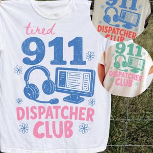 May include: A white t-shirt featuring a graphic print with the text "tired 911 DISPATCHER CLUB" in pink and blue. The design includes a blue illustration of a headset and a computer monitor, accented by small blue flower icons on the sides.
