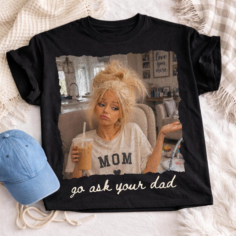 May include: Black t-shirt featuring a distressed image of a woman holding a drink, with the word "MOM" and the phrase "go ask your dad". A blue denim baseball cap is visible on the left.