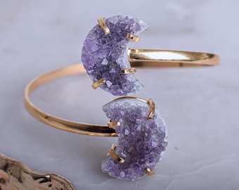 May include: A gold bangle bracelet with two amethyst crescent moon charms. The bracelet is open and the charms are facing the camera.