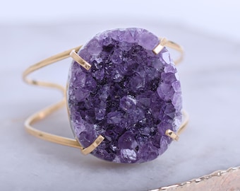 May include: A gold metal ring with a large, oval-shaped amethyst gemstone. The amethyst is a cluster of small, purple crystals.
