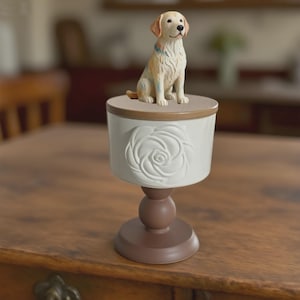 Peut inclure: Un r&eacute;cipient d&eacute;coratif sur pi&eacute;destal avec une figurine de golden retriever assis sur le dessus. Le r&eacute;cipient est blanc avec un bord et une base marron, et un motif de rose. La figurine de chien est de couleur beige et cr&egrave;me.