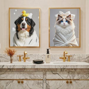May include: Two framed art prints featuring animals in a bathroom setting. One print shows a dog wearing a bathrobe and a rubber duck on its head. The other print shows a cat wearing a bow and a bathrobe.