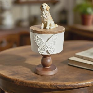 Peut inclure: Un r&eacute;cipient blanc cass&eacute; d&eacute;coratif avec un motif de papillon et un couvercle en bois. Une figurine de chien golden retriever est pos&eacute;e sur le couvercle. Le r&eacute;cipient est sur un pi&eacute;destal en bois.