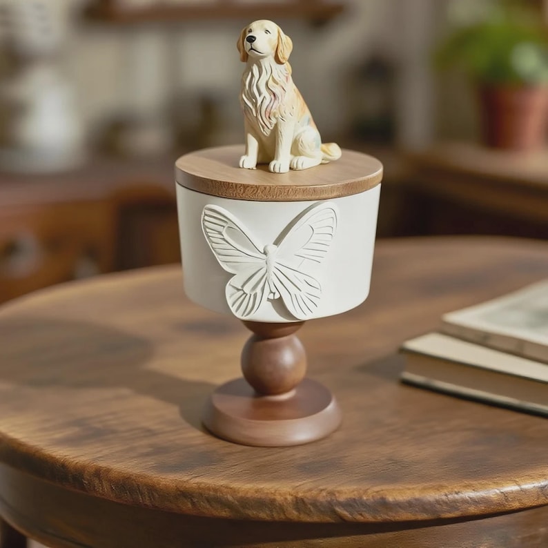 Peut inclure: Un r&eacute;cipient blanc cass&eacute; d&eacute;coratif avec un motif de papillon et un couvercle en bois. Une figurine de chien golden retriever est pos&eacute;e sur le couvercle. Le r&eacute;cipient est sur un pi&eacute;destal en bois.