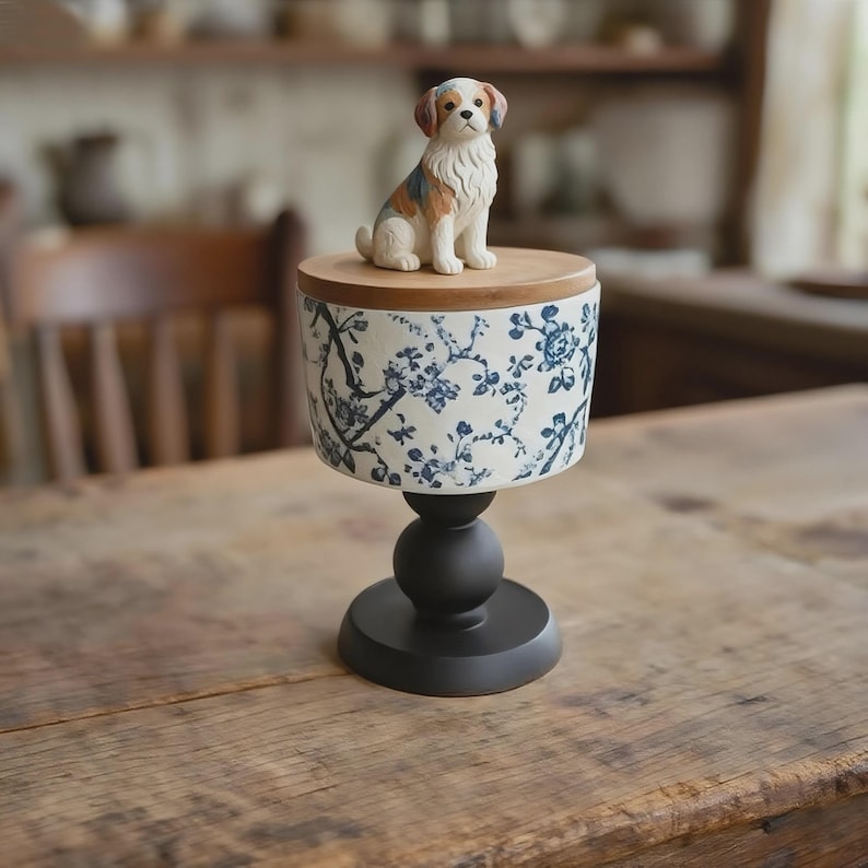 Peut inclure: Un pi&eacute;destal d&eacute;coratif avec un r&eacute;cipient en c&eacute;ramique orn&eacute; d'un motif floral bleu. Une petite figurine de chien est pos&eacute;e sur un couvercle en bois. Le pi&eacute;destal a une base noire et une section m&eacute;diane sph&eacute;rique, le tout reposant sur une table en bois.
