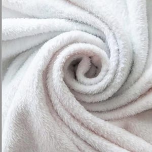 Könnte beinhalten: Nahaufnahme einer weißen und grauen Plüschdecke mit weicher, flauschiger Textur. Die Decke ist gefaltet und aufgerollt, wodurch die flauschigen Fasern sichtbar werden.