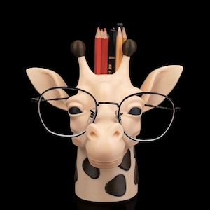 May include: A whimsical giraffe-shaped pencil holder, sporting black-rimmed glasses. The holder is beige with brown spots and holds several pencils. The giraffe's head is the main focus against a black background.