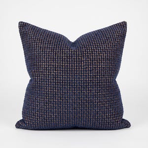 May include: A square throw cushion featuring a deep navy blue and tan woven fabric with a distinct grid-like texture. The material displays a repeating pattern of vertical and horizontal threads, creating a structured, tactile surface across the entire front.