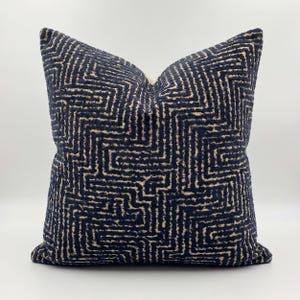 Op de afbeelding: Een vierkant decoratief kussen met een marineblauw en beige geometrisch patroon. Het kussen heeft een getextureerd oppervlak en een zachte uitstraling. Het patroon heeft een doolhofachtig ontwerp, wat visuele interesse toevoegt aan de interieurdecoratie.