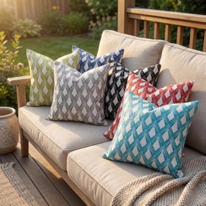 Puede incluir: Conjunto de cojines decorativos con estampado de rombos en varios colores: verde, azul, gris, negro y rojo. Los cojines están colocados sobre un sofá beige de exterior, creando un ambiente acogedor.