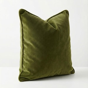 May include: A square olive green velvet cushion. The cushion has a soft, plush texture and a classic design. The cushion is a solid colour and has a simple, elegant look. A decorative item for a bed or sofa.