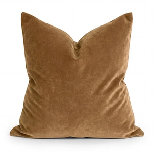 May include: A square, brown velvet pillow with a soft, plush appearance. The pillow has a classic shape and is designed for comfort and style. The color is a warm, earthy tone, suitable for various interior design schemes.