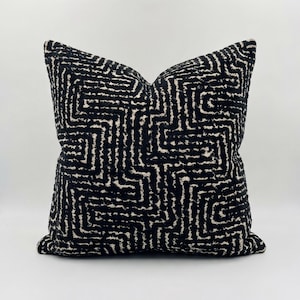 Può includere: Cuscino quadrato decorativo con un motivo geometrico nero e bianco sporco. Il motivo presenta un design a labirinto. Il cuscino ha una superficie strutturata e un aspetto morbido.