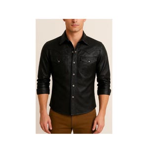 Puede incluir: Una camisa negra de manga larga con cuello en punta, cierre frontal de botones y dos bolsillos en el pecho con solapa. La camisa presenta canesúes de estilo western en los hombros delanteros y botones metálicos en la tapeta central.