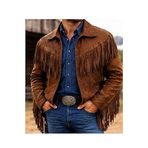 May include: A brown suede jacket featuring long fringe detailing across the chest and sleeves, paired with a blue button-down shirt and blue jeans with a large silver belt buckle. The jacket has a classic collar and a front zipper closure.
