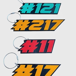 May include: Four keychains with black, white, and colored numbers on a white background. The numbers are #121, #217, #11, and #17. Each keychain has a silver metal ring.