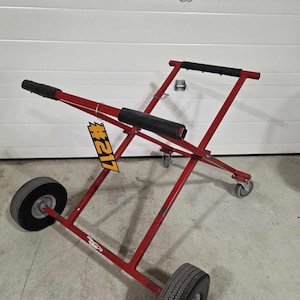 May include: Red metal cart with black handles and four wheels. The cart is designed to transport large items. A yellow tag with the number #121 is attached to the cart.