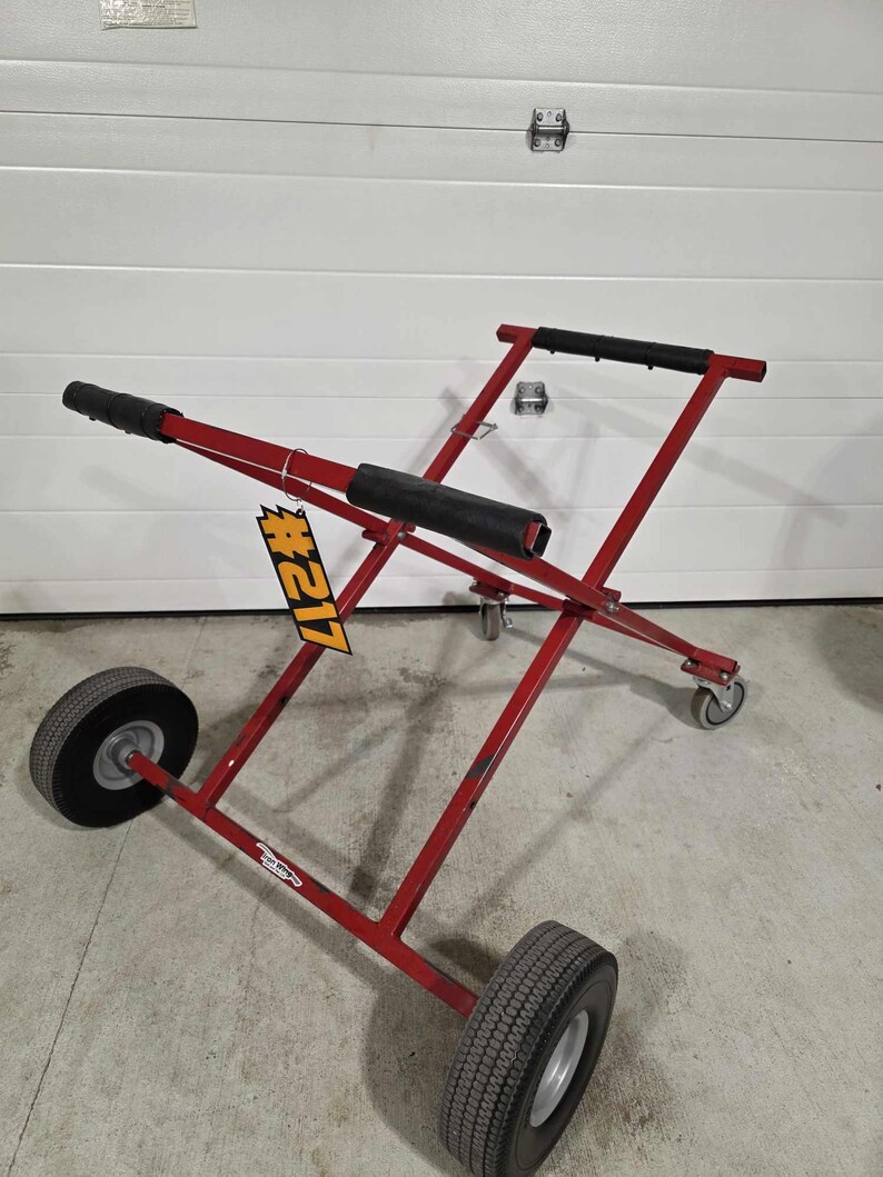 May include: Red metal cart with black handles and four wheels. The cart is designed to transport large items. A yellow tag with the number #121 is attached to the cart.