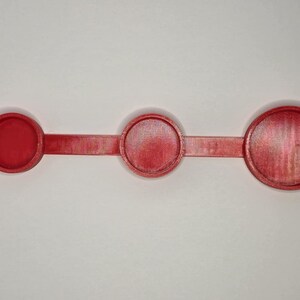 Puede incluir: Un juego de cucharas medidoras de pl&aacute;stico rojo. Cuenta con tres tazas medidoras circulares de diferentes tama&ntilde;os, conectadas por un mango plano y delgado. El juego est&aacute; sobre un fondo blanco.