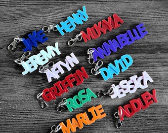 May include: A collection of colorful personalized keychains with names including Jake, Henry, Mikaya, Annabelle, Jeremy, Aftin, Griffin, David, Rosa, Jessica, Marlie, and Addley.