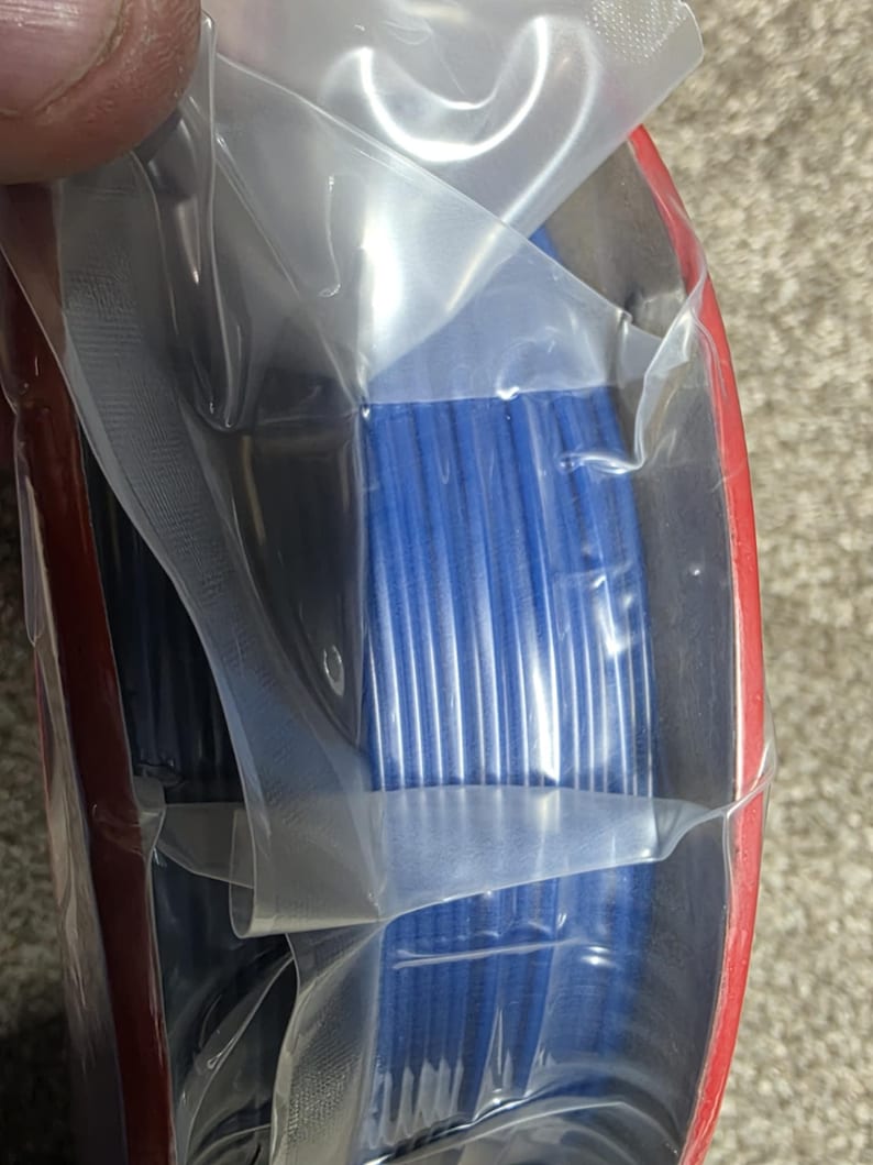 May include: A spool of blue filament for 3D printing is wrapped in clear plastic and packaged in a red box.