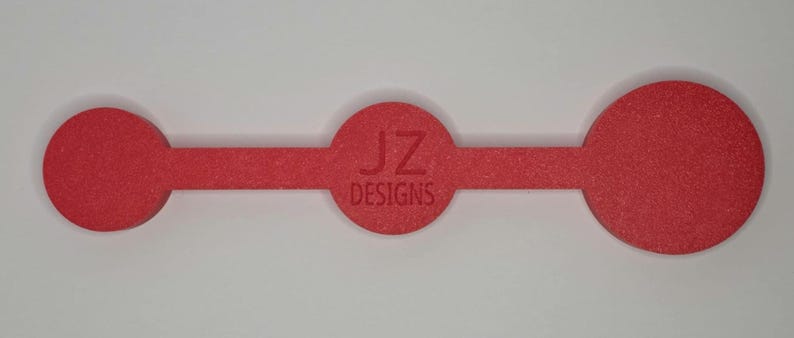 Puede incluir: Un elemento de dise&ntilde;o rojo texturizado, horizontal, con tres componentes circulares conectados por una barra rectangular estrecha. El c&iacute;rculo central presenta el texto "JZ DESIGNS" en rojo m&aacute;s oscuro. El dise&ntilde;o est&aacute; sobre un fondo blanco.