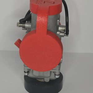 Puede incluir: Un componente mec&aacute;nico plateado con una cubierta roja. La cubierta tiene el texto blanco "DESIGNS" y "7L". Tambi&eacute;n se ven un cable negro y una base negra.