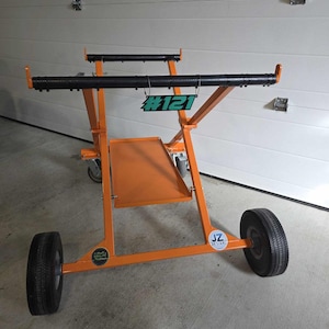 May include: Orange metal cart with black bars and wheels. The cart has a number tag that says #121.