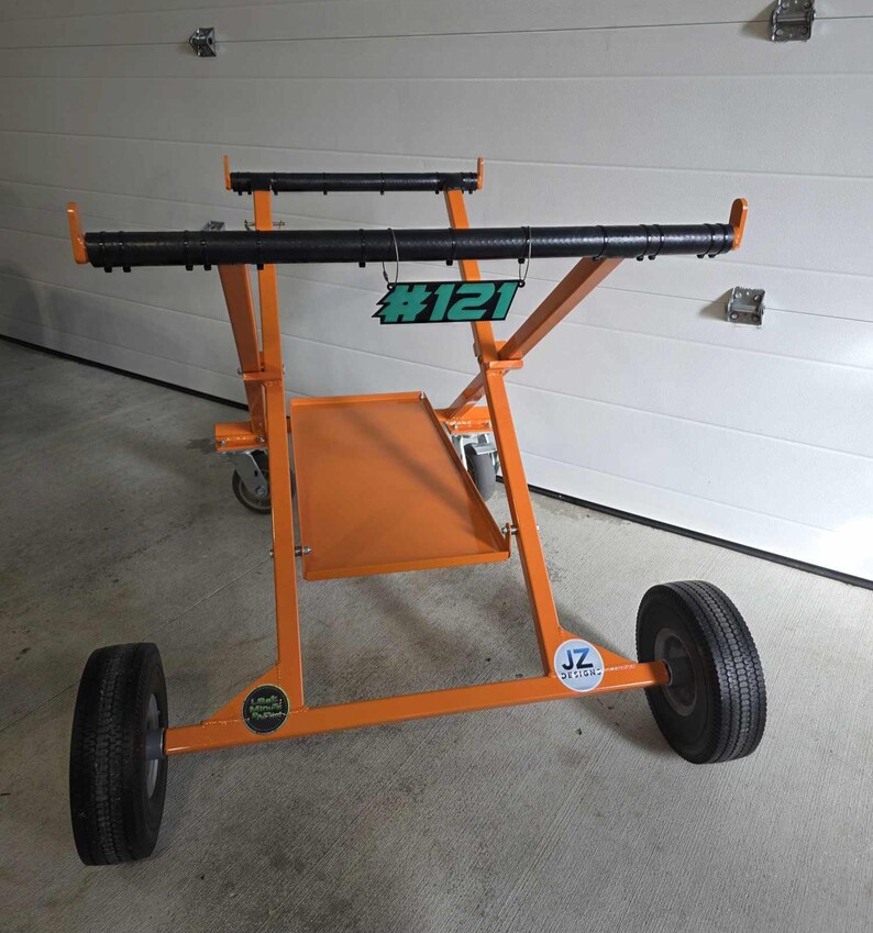 May include: Orange metal cart with black bars and wheels. The cart has a number tag that says #121.